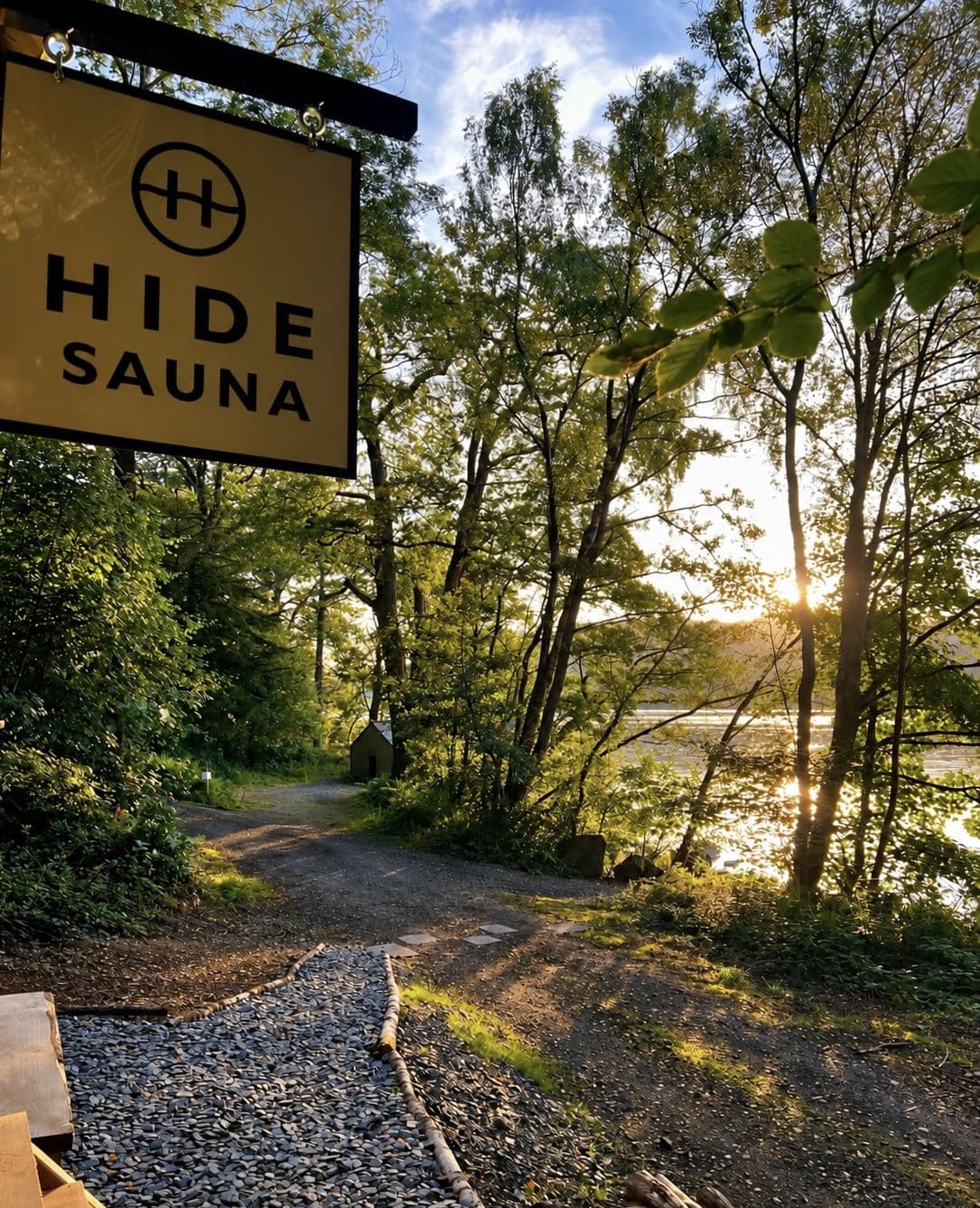 The hanging HIDE SAUNA sign beside the path, evening light coming through the lakeside trees behind it
